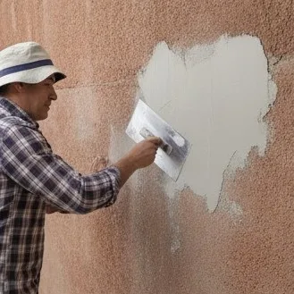 Albanil humedeciendo una pared con revoque grueso antes de aplicar la capa fina.